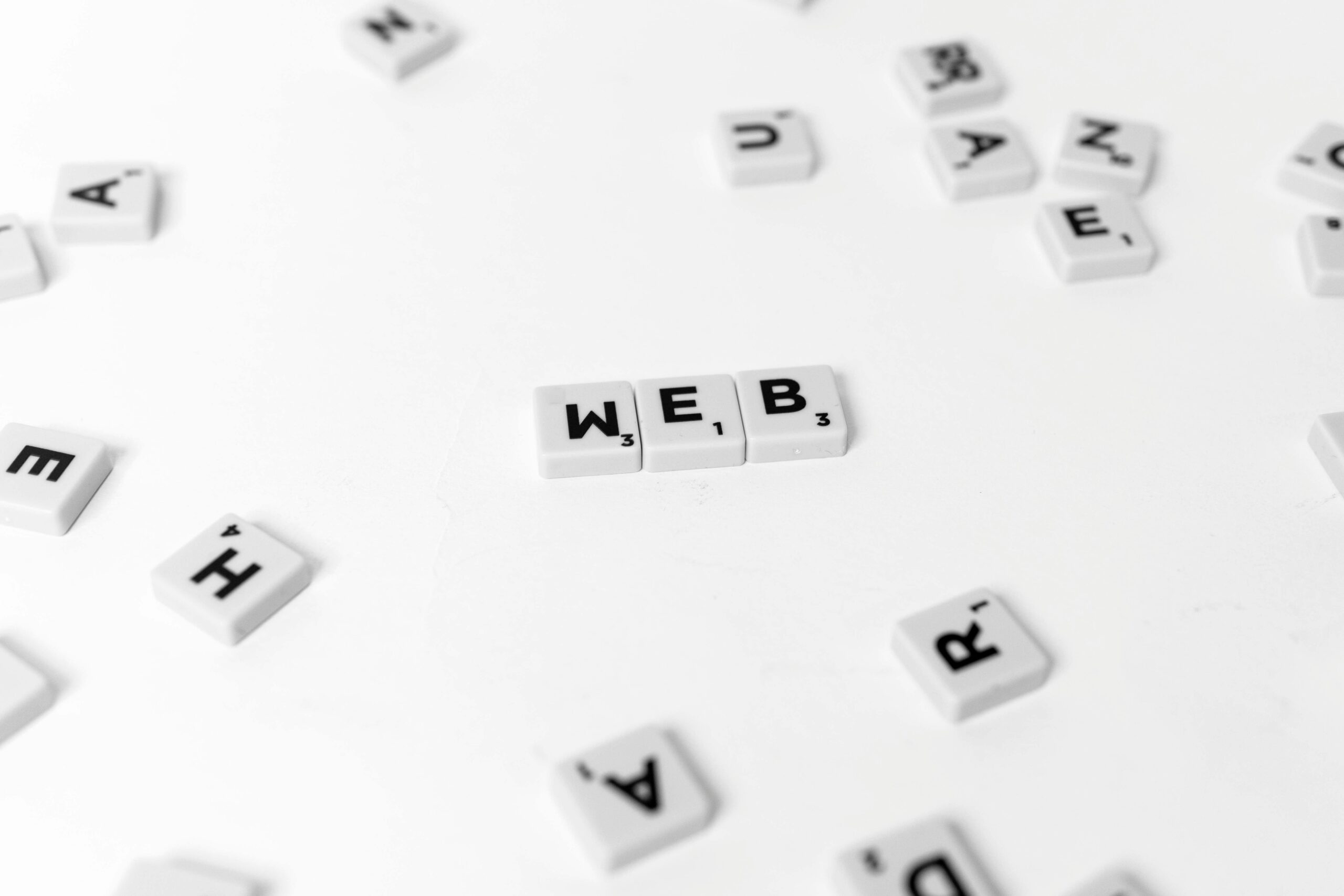 Scattered Scrabble tiles emphasize the word 'WEB' on a minimalist white background.
