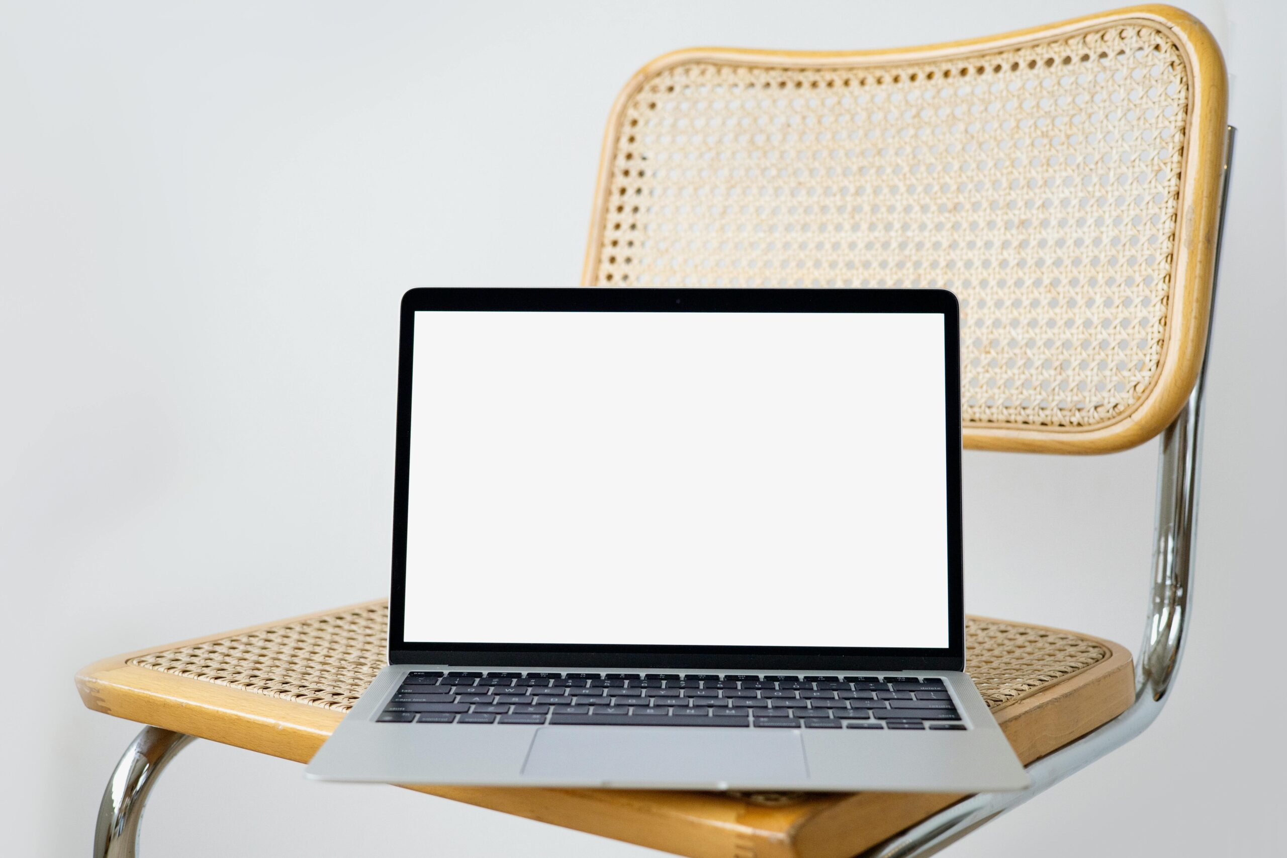 Modern laptop with a blank screen on a woven chair, perfect for digital presentations.